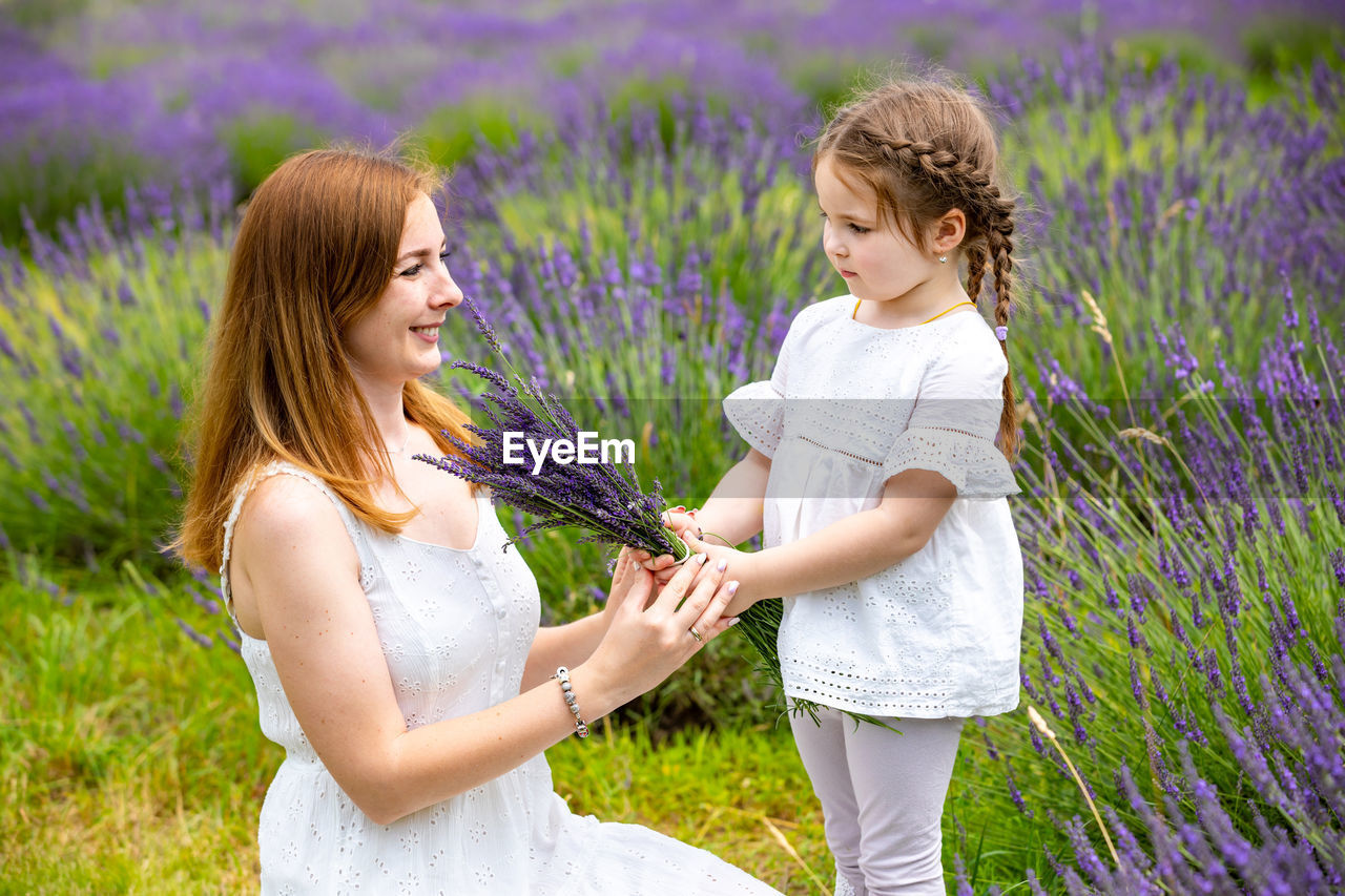 View of mother and girl by purple flowering plants on field