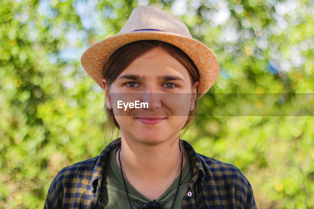 Close-up light smiling young brunette caucasian woman in hat. summer blurred green nature bokeh