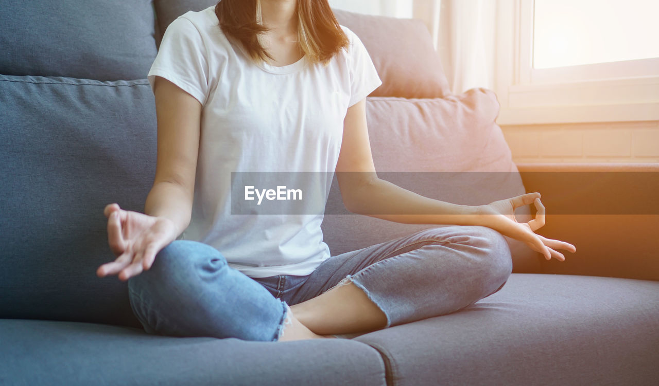 REAR VIEW OF WOMAN SITTING ON SOFA AT HOME