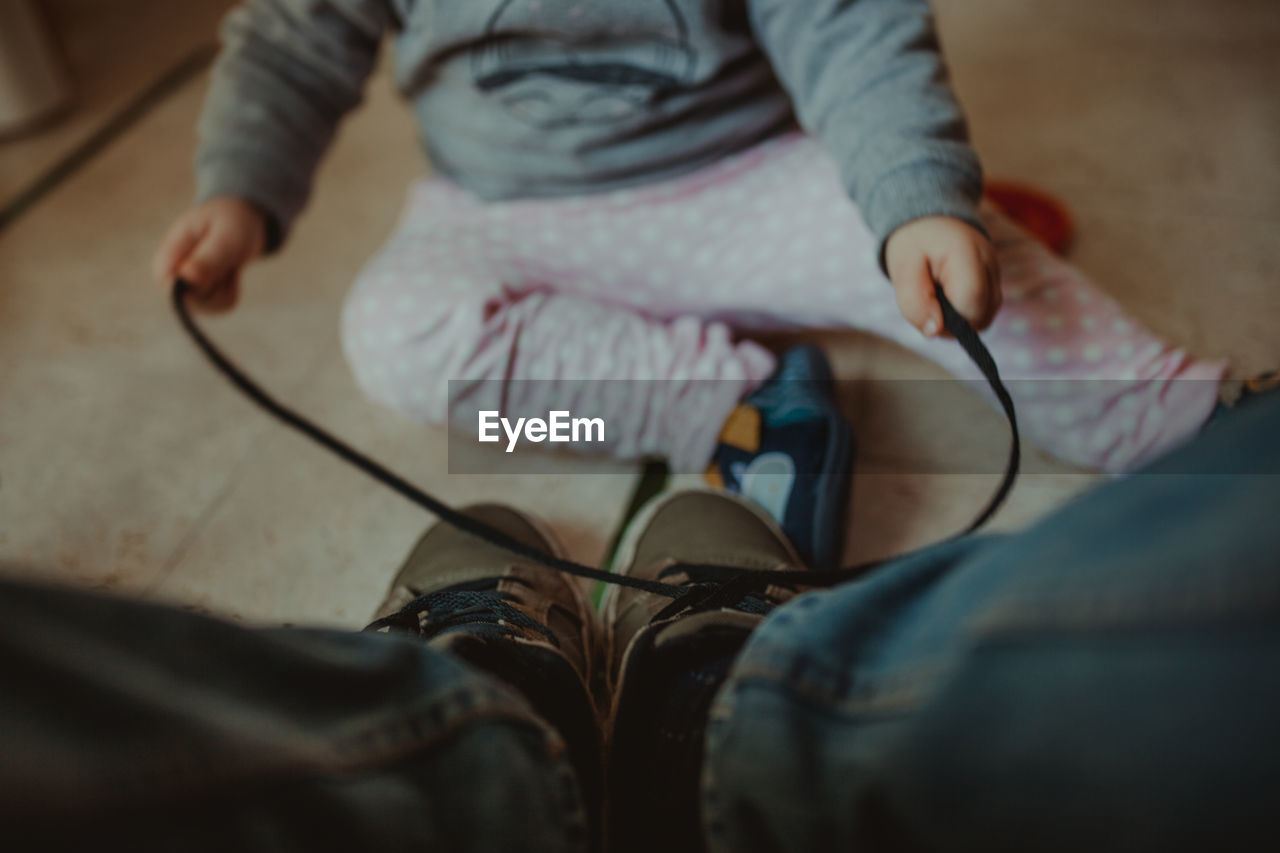 Low section of baby tying man shoelace on floor