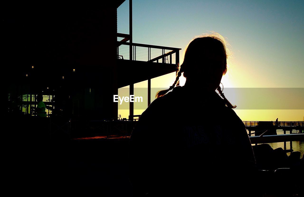 Rear view of silhouette girl on walkway at sunset