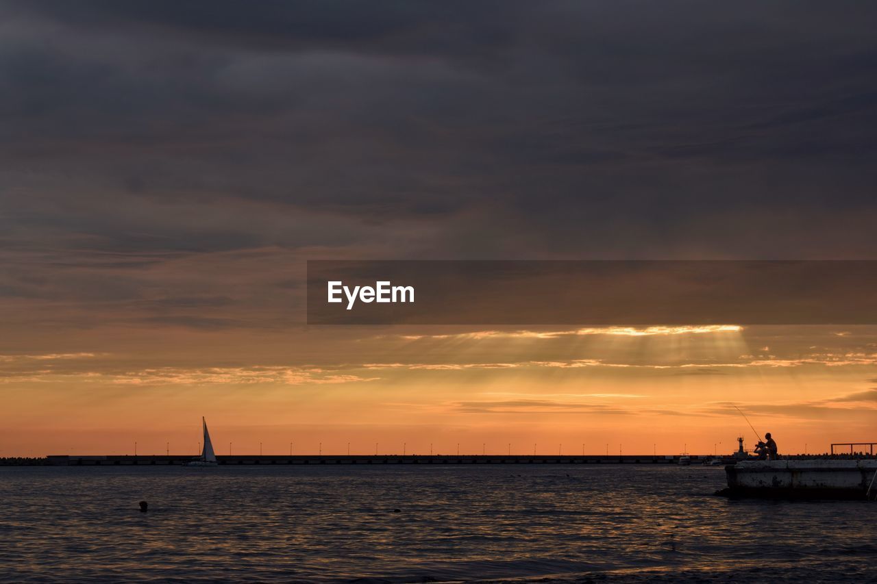 Silhouette sailboat sailing on sea against dramatic sky