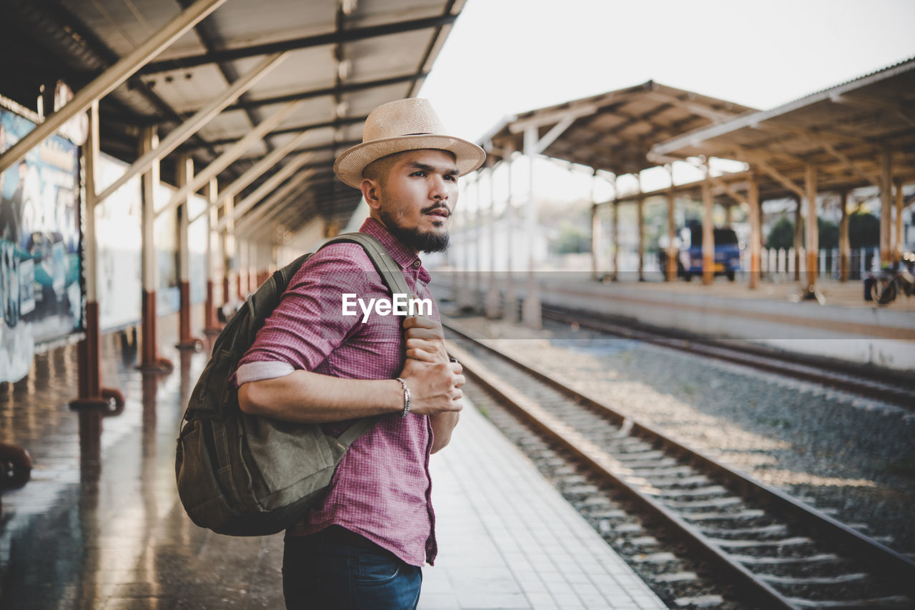 Side view of man with backpack standing at railroad station
