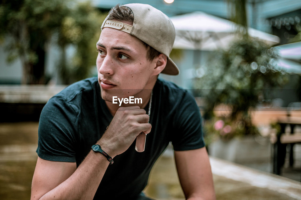 Thoughtful young man wearing cap while sitting outdoors