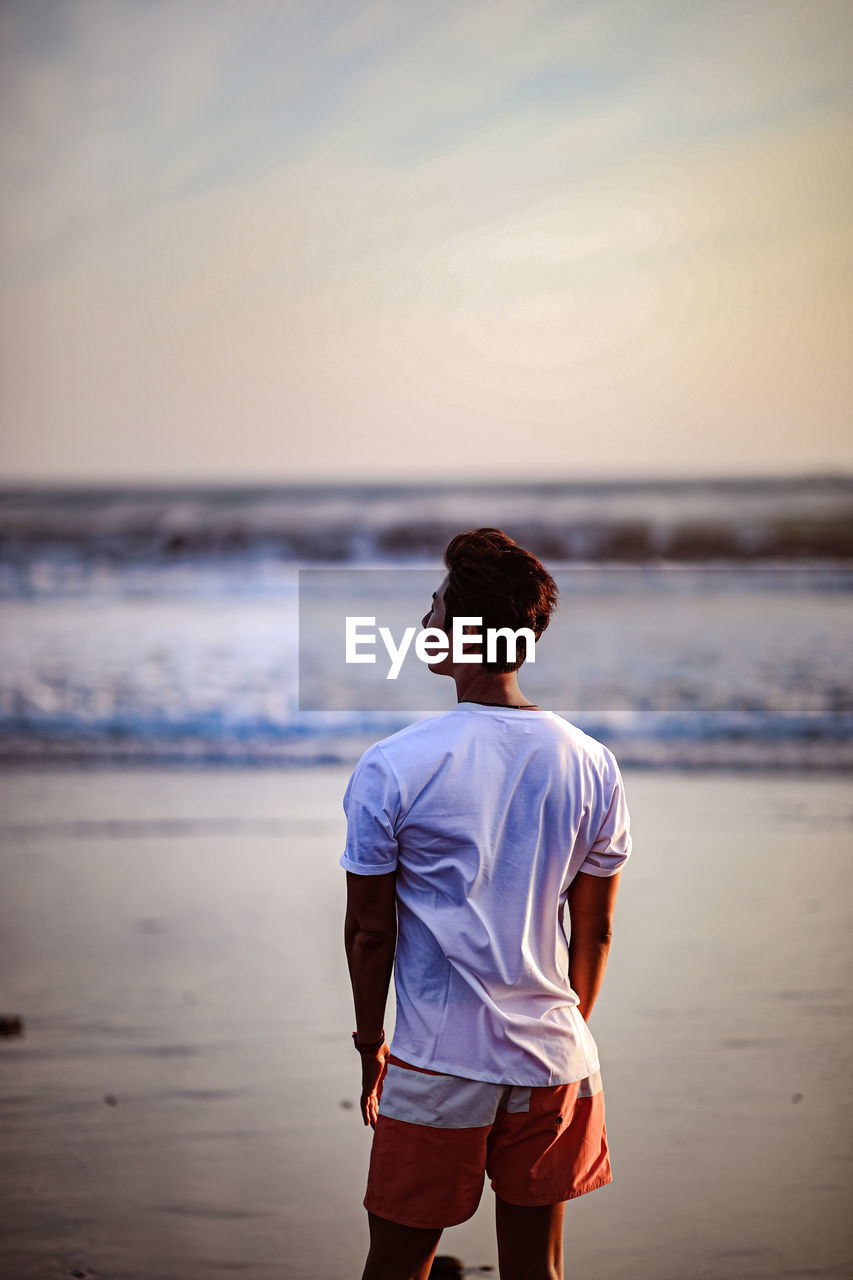 Man standing on beach against sky during sunset