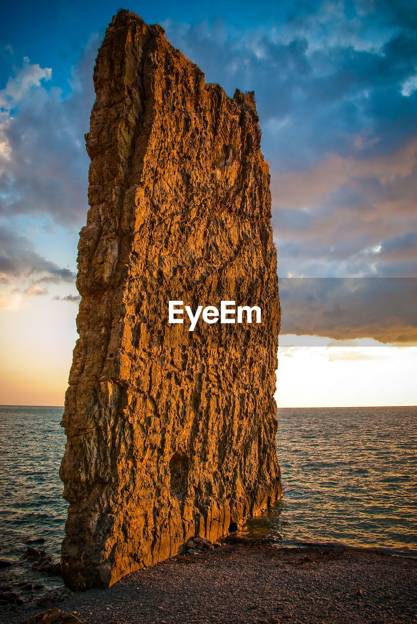 Sail rock on coastline of black sea against cloudy sky during sunset