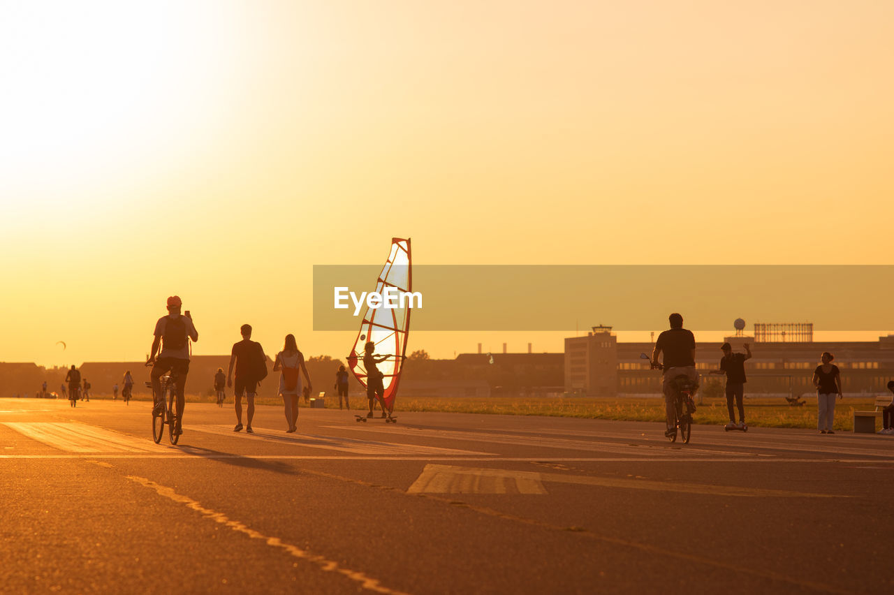 PEOPLE WALKING ON ROAD AGAINST CLEAR SKY DURING SUNSET