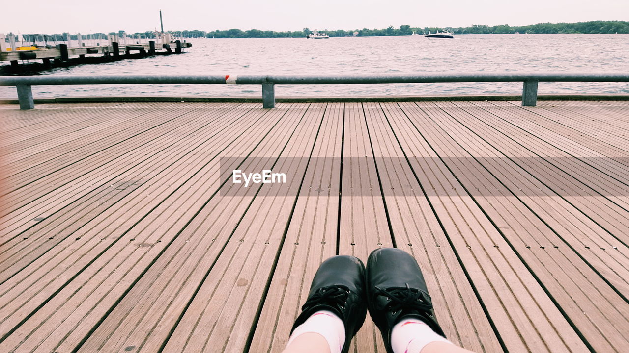 Low section of person relaxing on pier over river