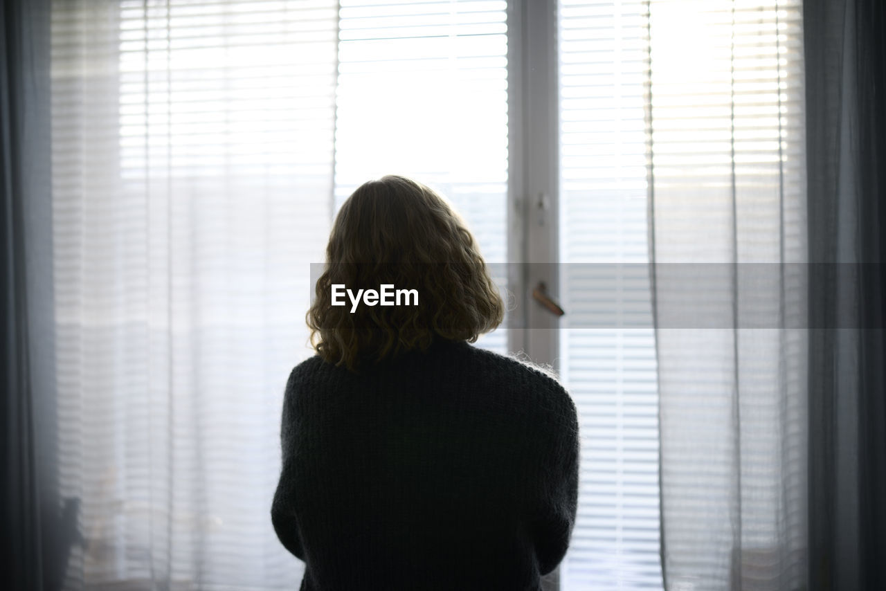 Rear view of teenage girl looking through window