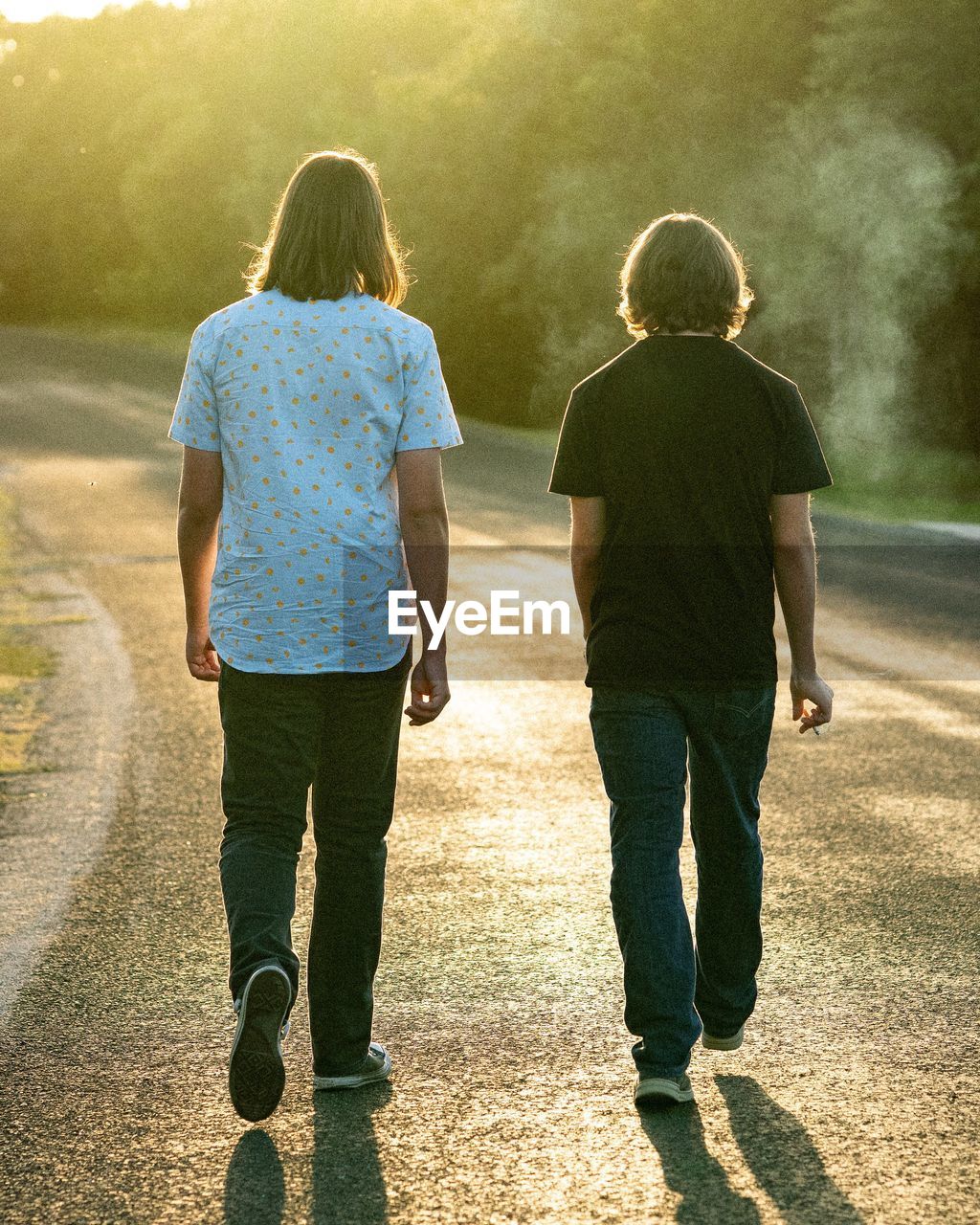 REAR VIEW OF TWO PEOPLE WALKING ON ROAD