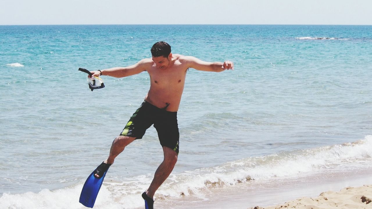 Full length of shirtless man with diving flippers at beach