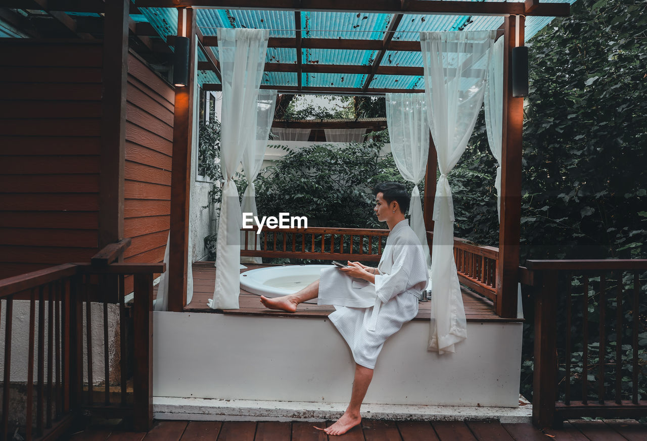 Young man wearing bathrobe sitting by hot tub