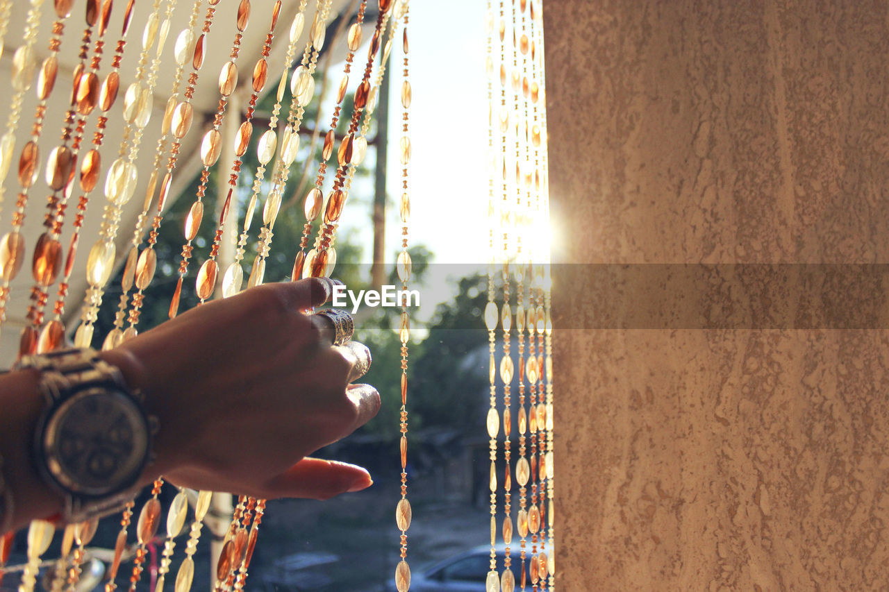 Hand of woman holding beaded curtain by wall