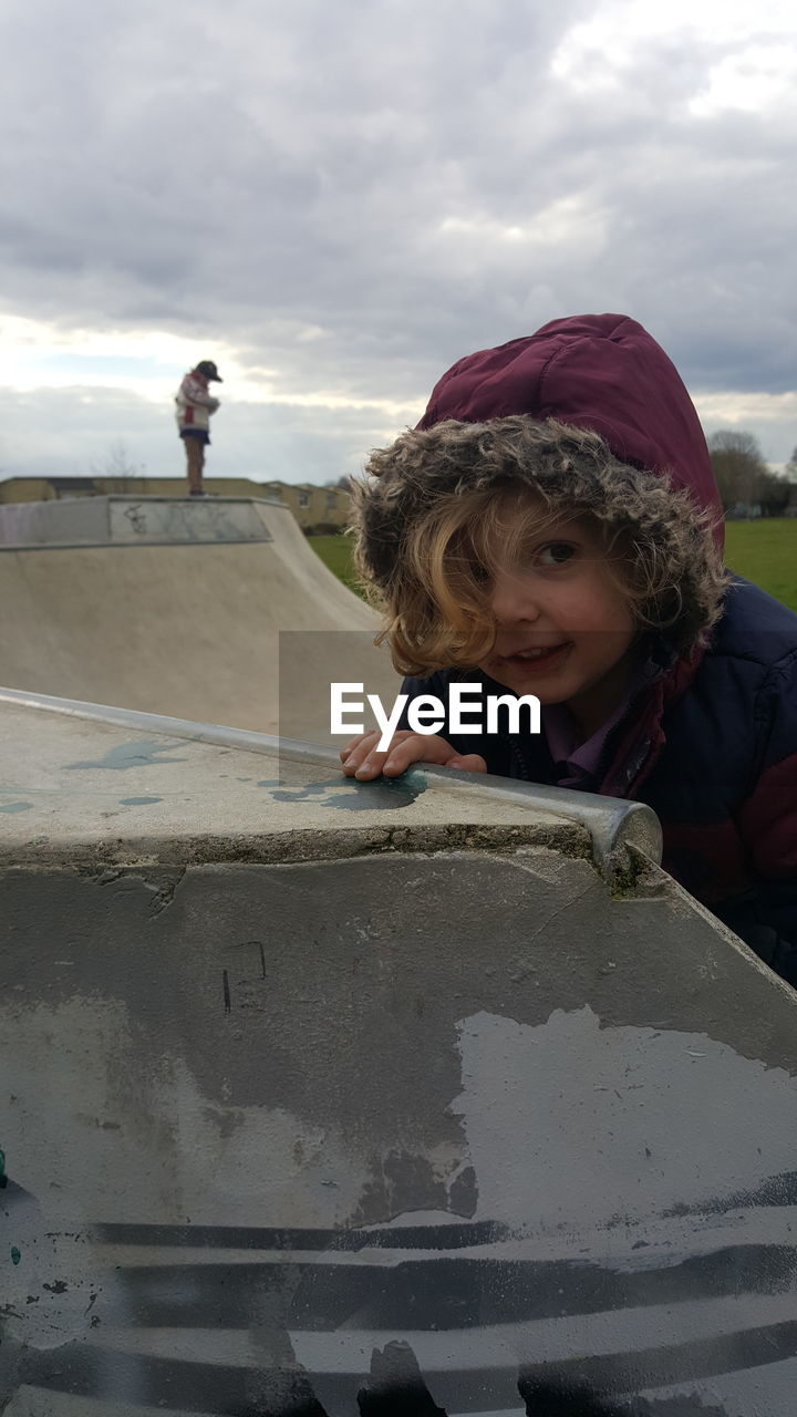 Portrait of cute girl standing by sports ramp against cloudy sky at park