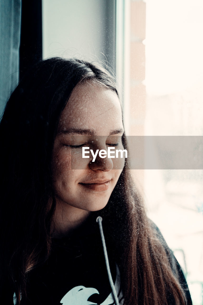 Close-up of woman with eyes closed by window at home