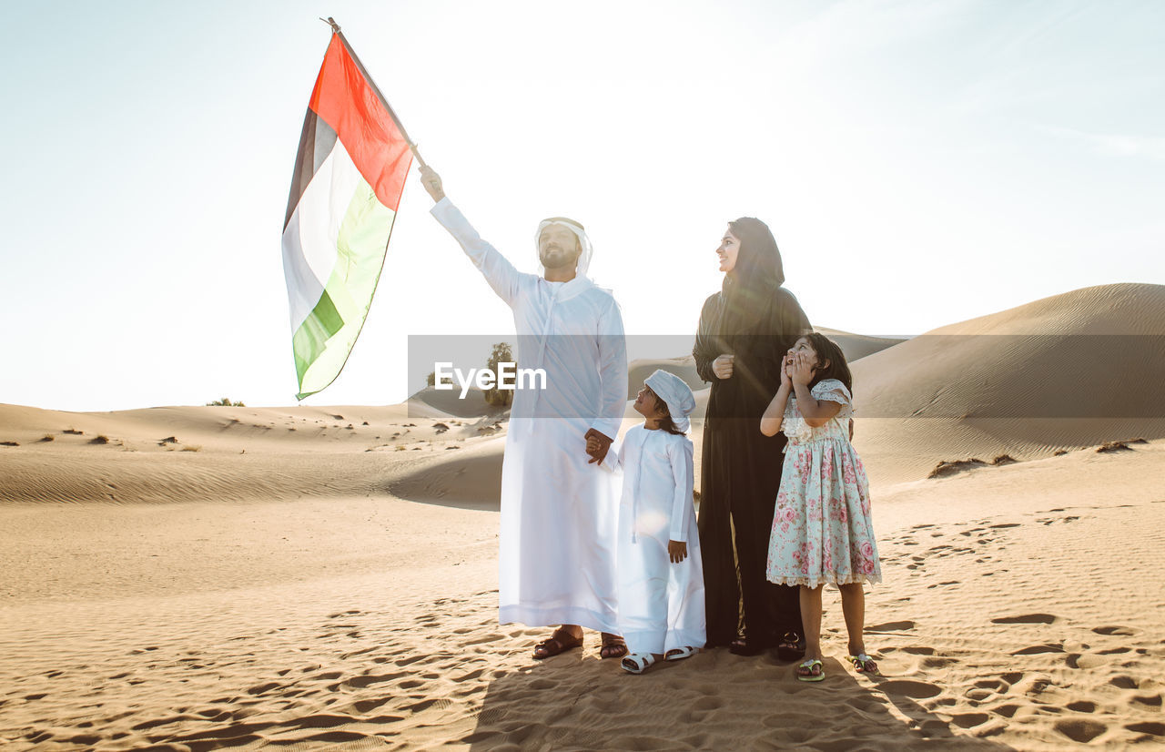Arabian family holding flag while standing at desert against sky