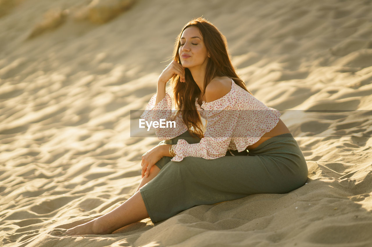 Young woman blowing kiss while sitting on beach