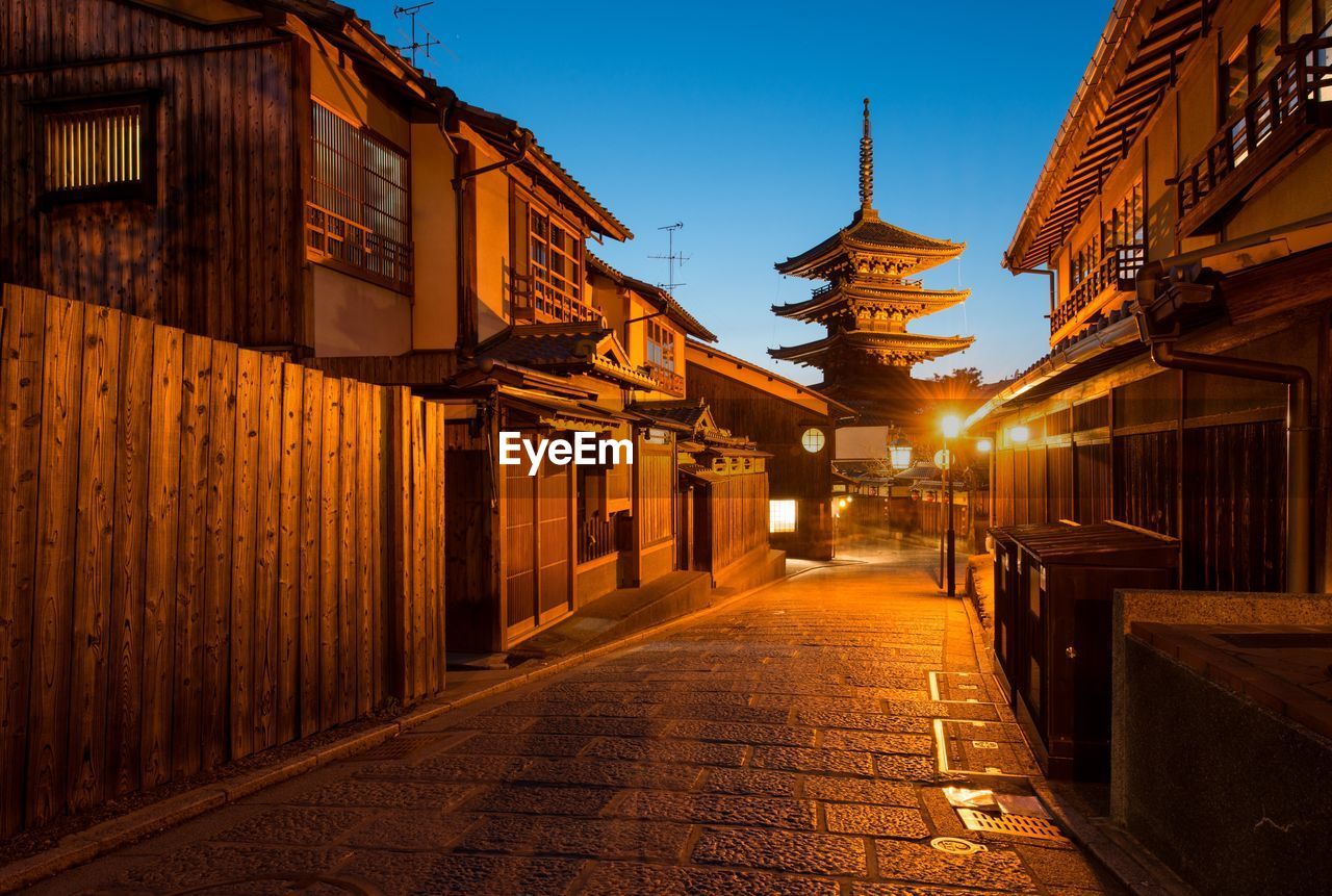 ILLUMINATED STREET AMIDST BUILDINGS AGAINST SKY