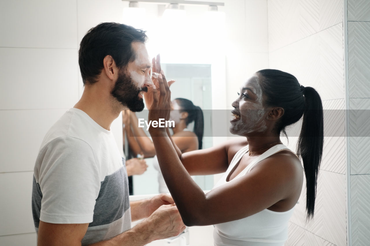 Side view of woman applying face mask to man at home