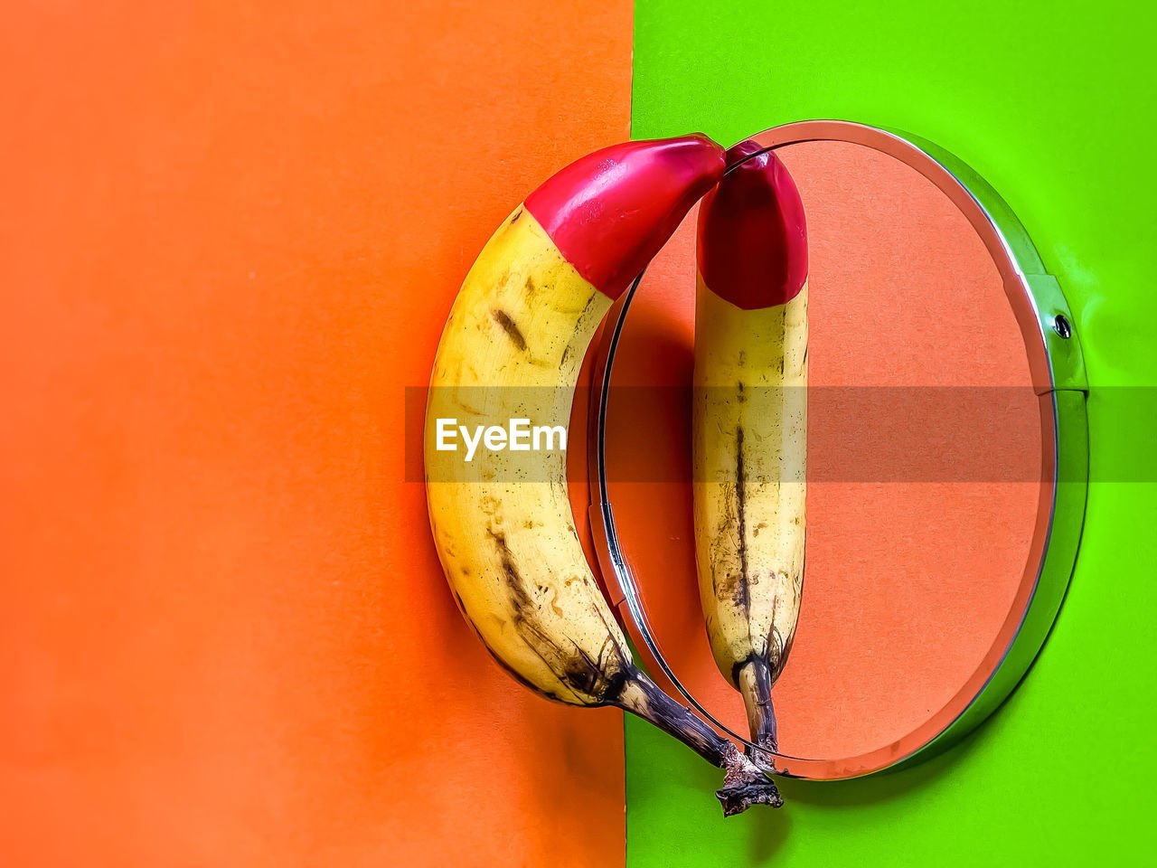 High angle view of red tipped banana on mirror on orange and green background.