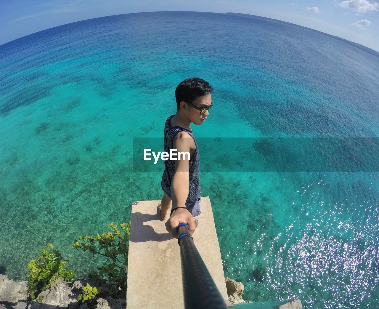 Fish-eye lens of young man with monopod standing on pier over sea