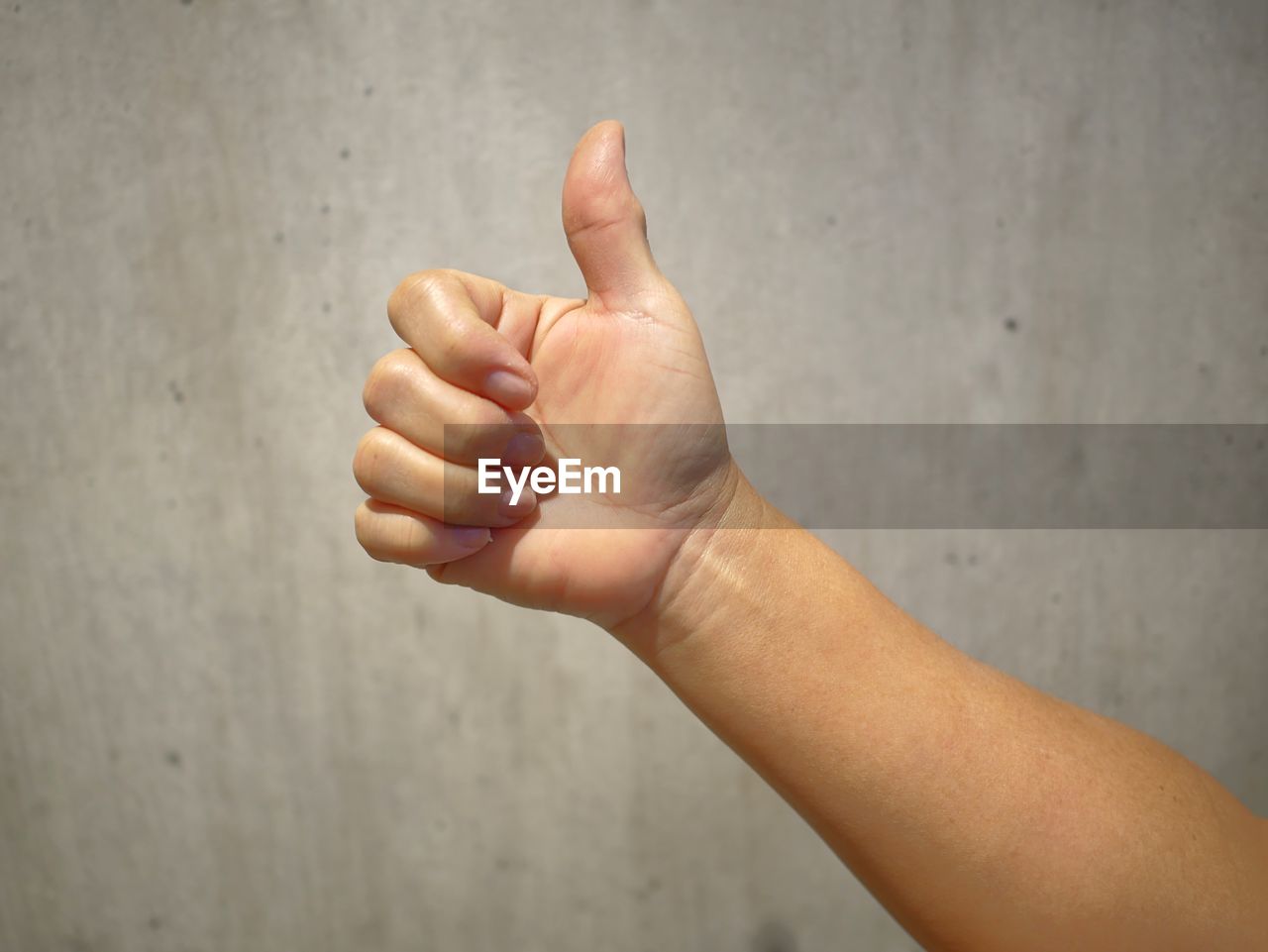 Close-up of hand gesturing thumbs up against wall