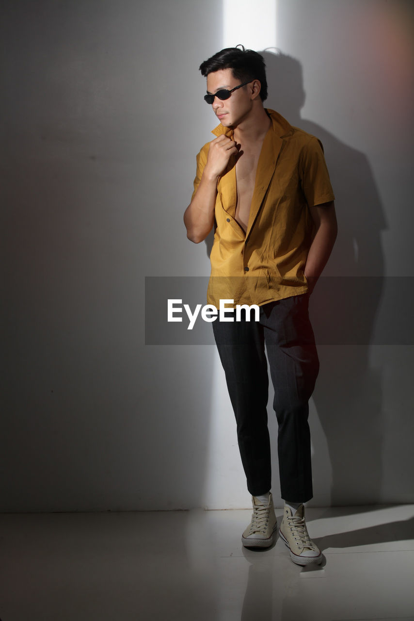 Young man looking away while standing against wall