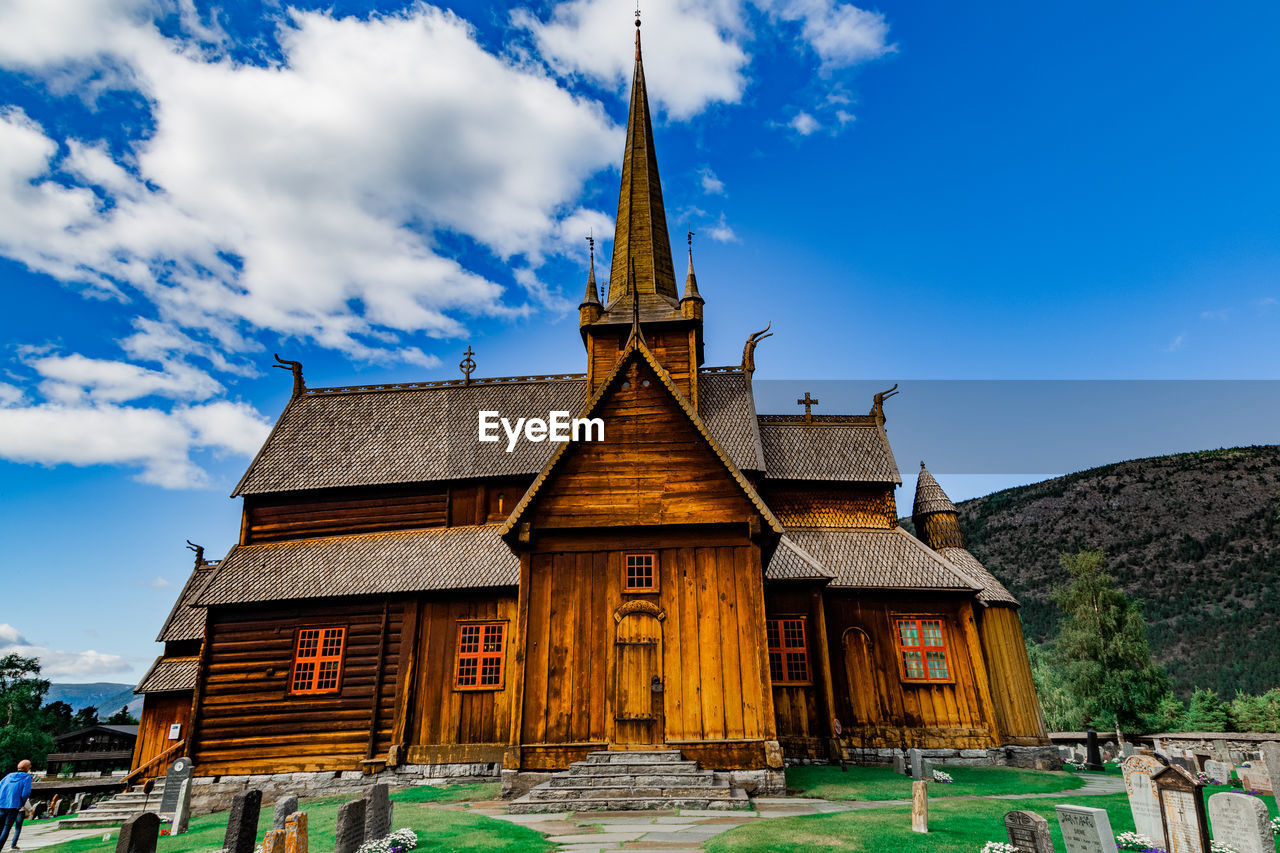 View on the cemetery, medieval stave church in lom, mountains against cloudy sky on a sunny day
