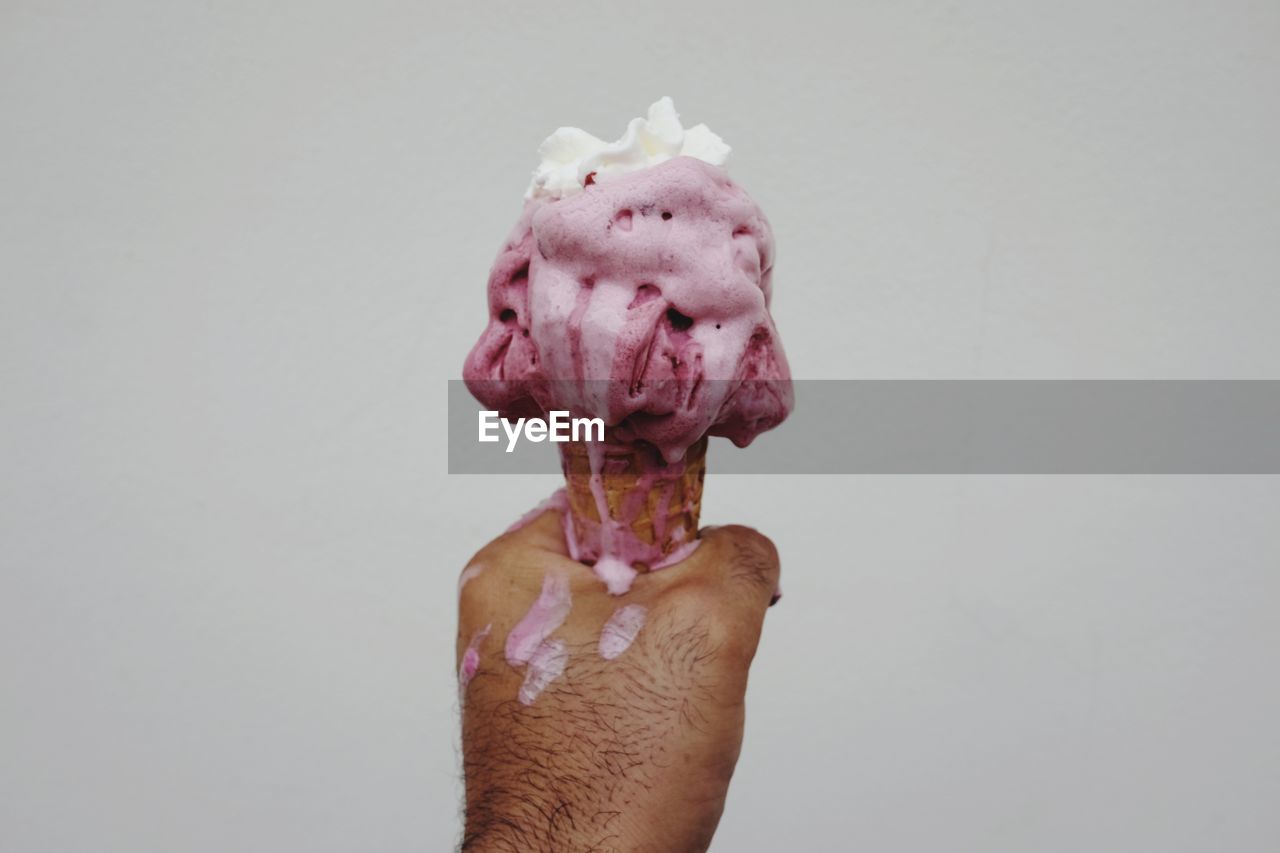 Cropped hand of man holding ice cream cone against white background