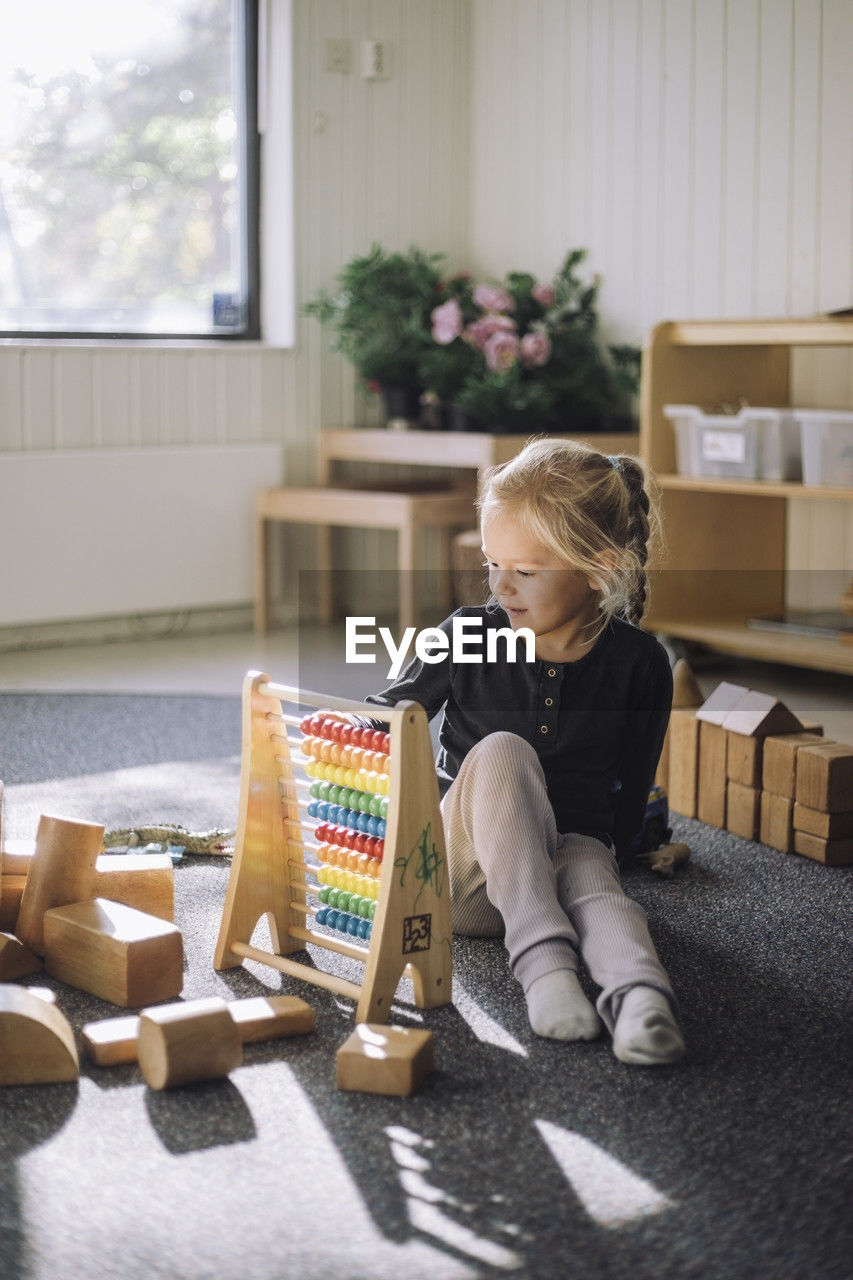 Girl learning to count through abacus while sitting in classroom at kindergarten