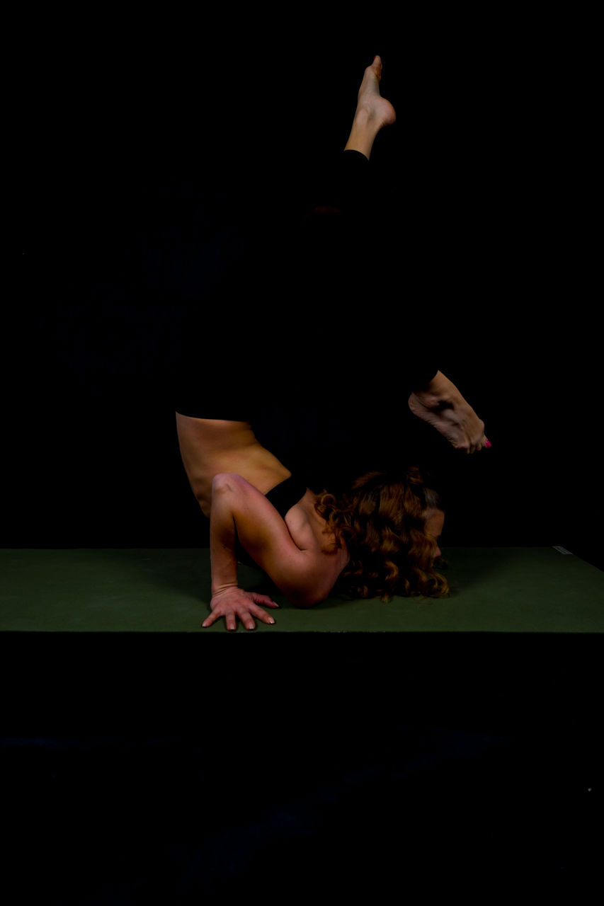 Side view of woman exercising against black background