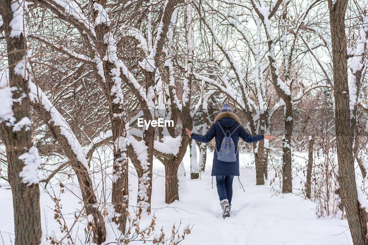 Rear view of woman wearing warm clothing with backpack walking on snow in forest