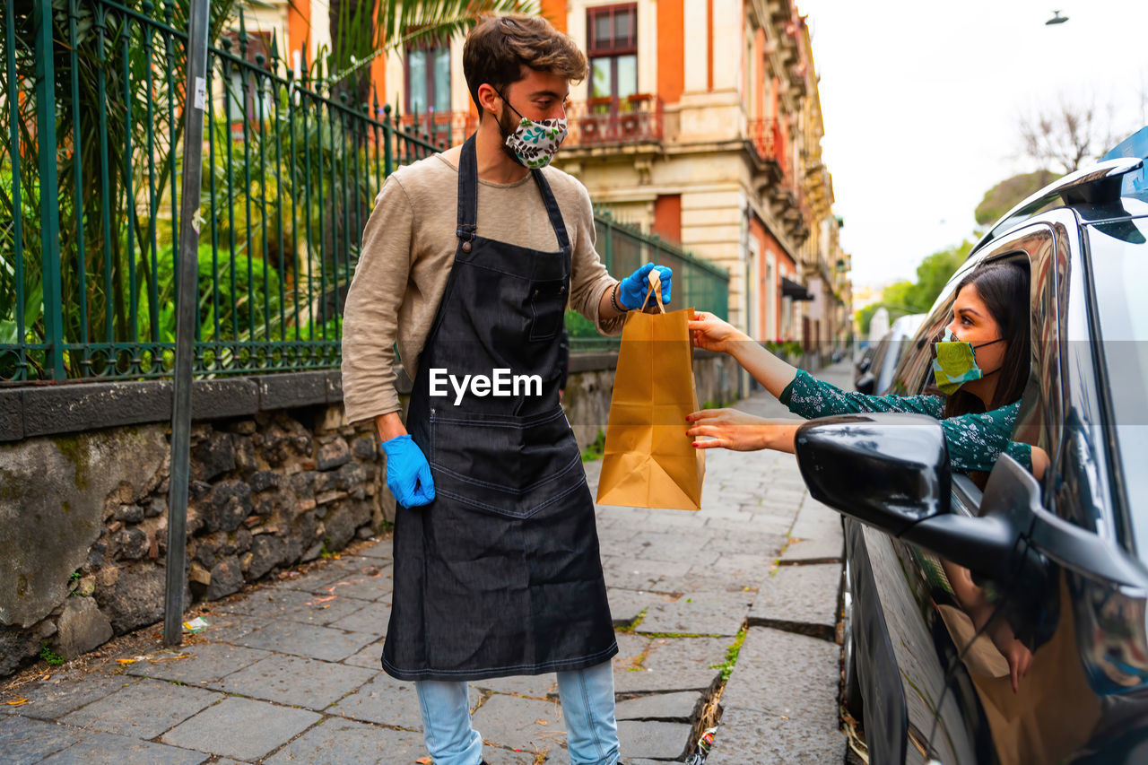 Closeup hipster delivery man wearing medical protective, holding paper shopping bags in hands. 