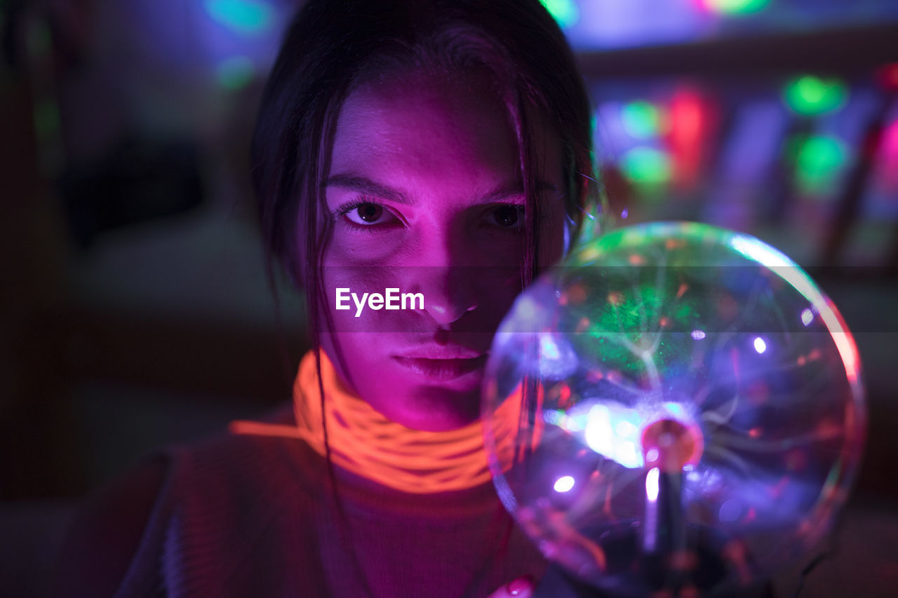 Close-up portrait of woman wearing illuminated necklace holding lighting equipment in darkroom