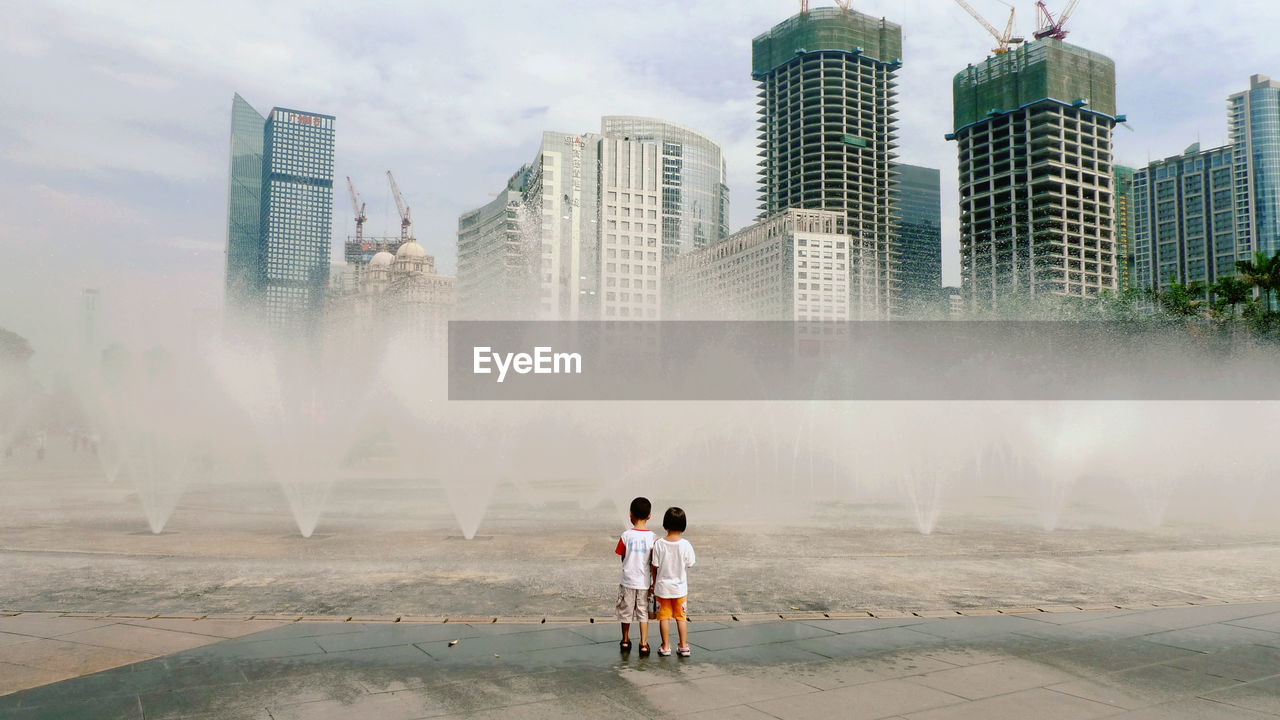 REAR VIEW OF PEOPLE STANDING BY MODERN CITYSCAPE