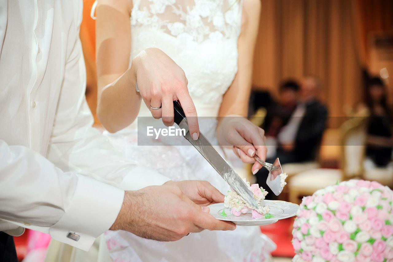 Midsection of bride holding knife with cake on plate by waiter