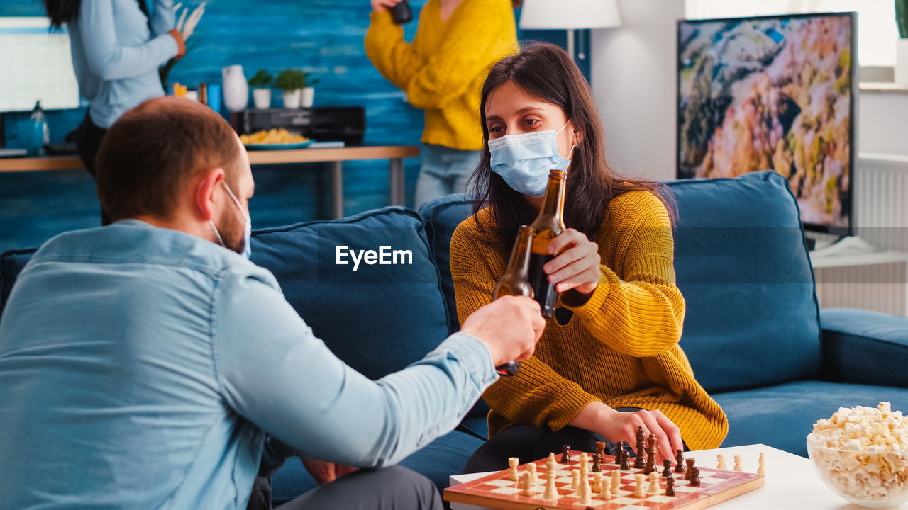 Man and woman drinking beer while playing chess at home