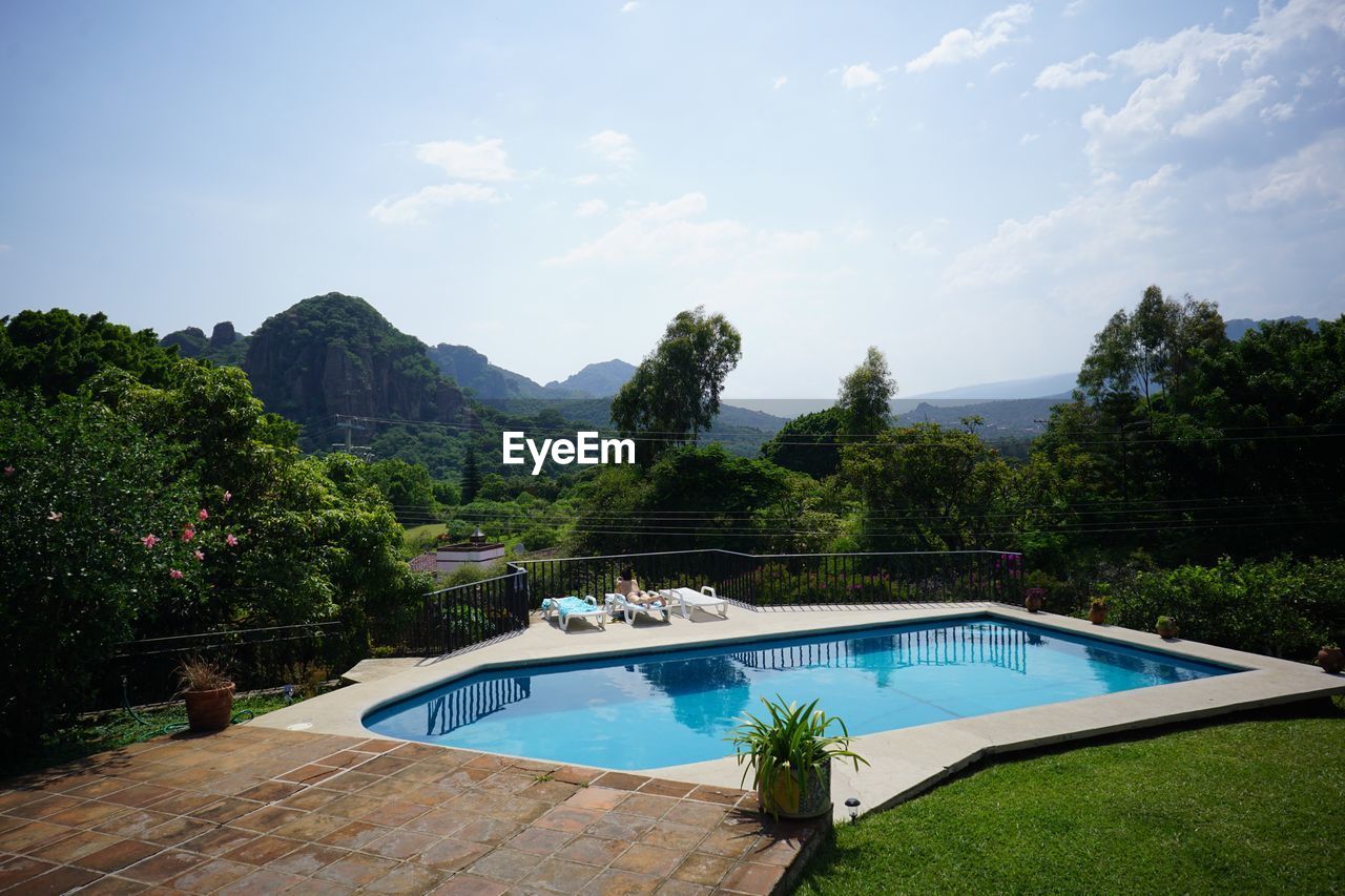 Swimming pool by trees against sky