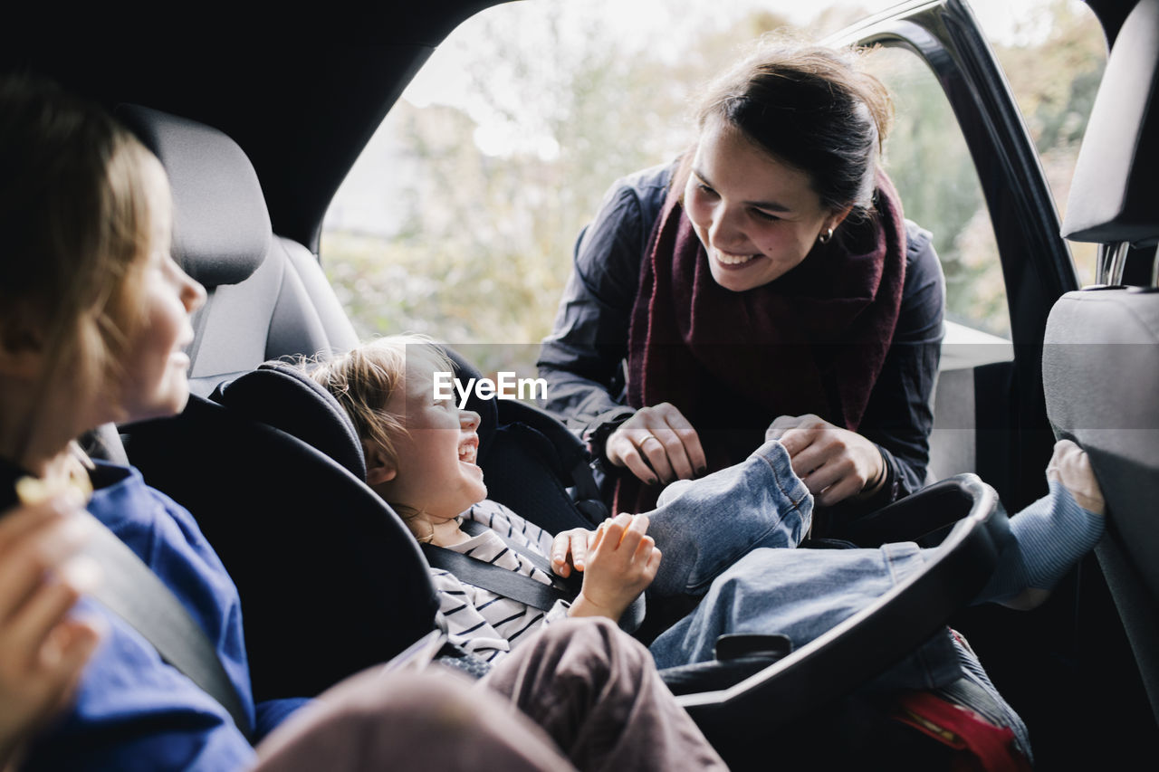 Happy mother tickling daughter sitting in car