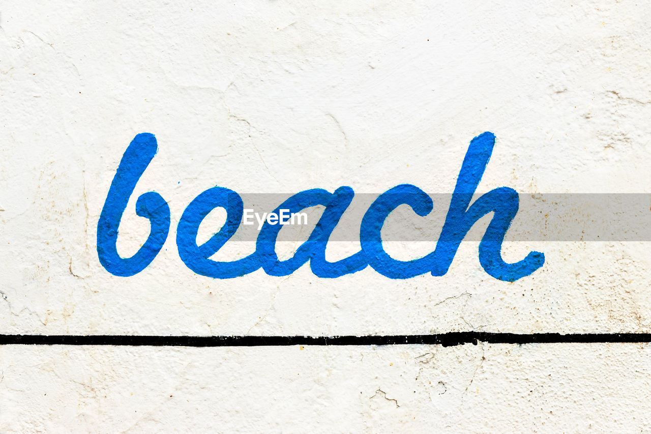Blue beach sign painted on a white wall. horizontal image.