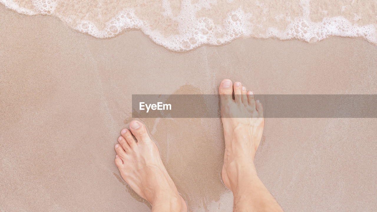 Feet stands on the beach sand with little sea wave in vacation time, relaxing and traveling concept