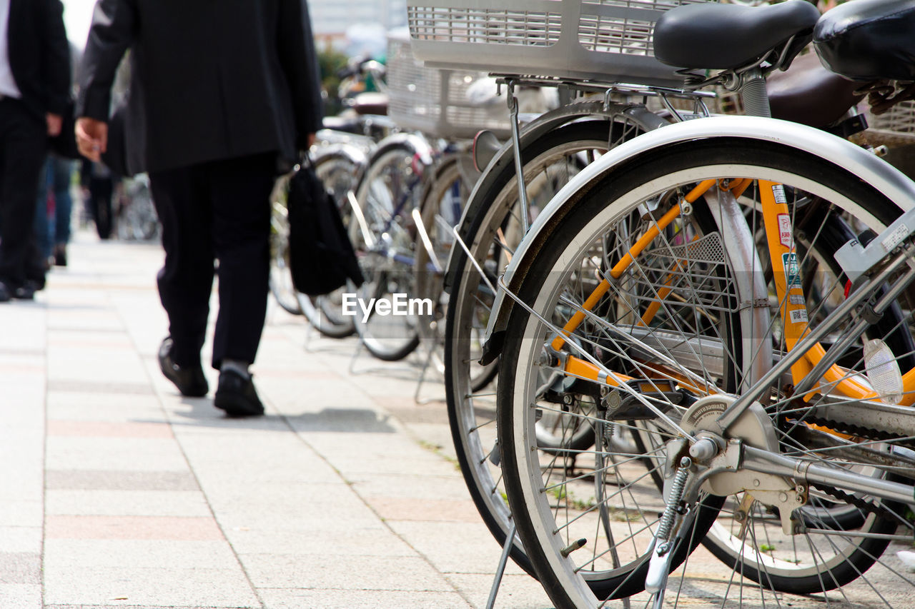 Low section of businessman walking on footpath by bicycles