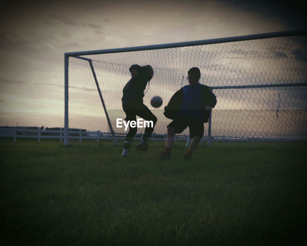 Boy and girl playing soccer against goal post