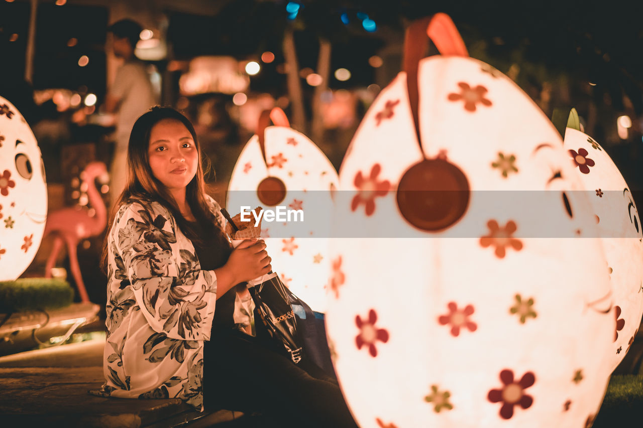 Full length portrait of smiling woman holding illuminated lighting equipment