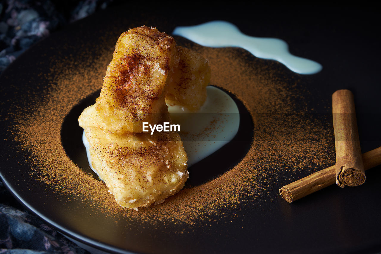 Traditional spanish dessert of fried milk with cinnamon and condensed milk on black plate