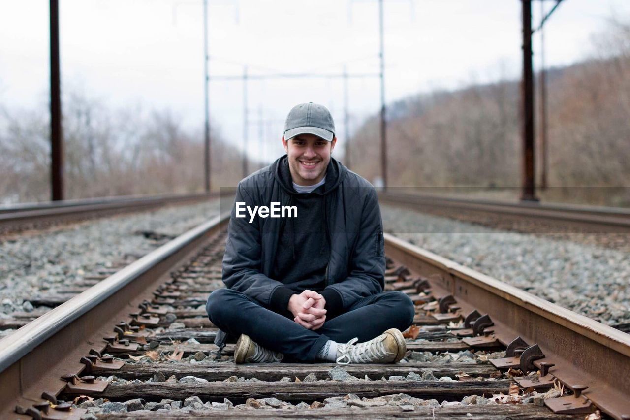 Portrait of happy young man sitting on railroad track
