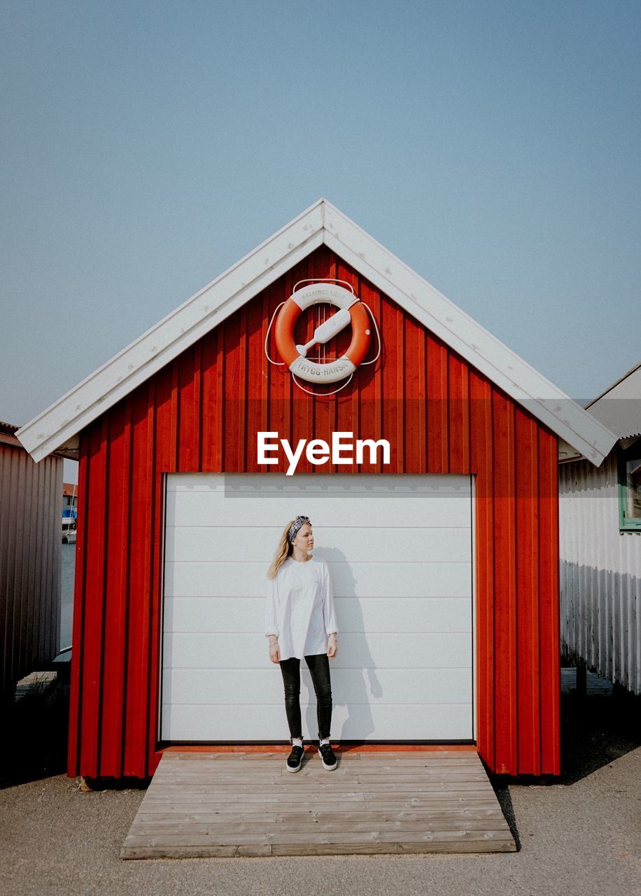 WOMAN STANDING ON RED BUILDING AGAINST SKY