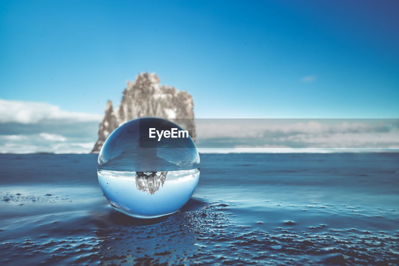 Crystal ball at beach against blue sky