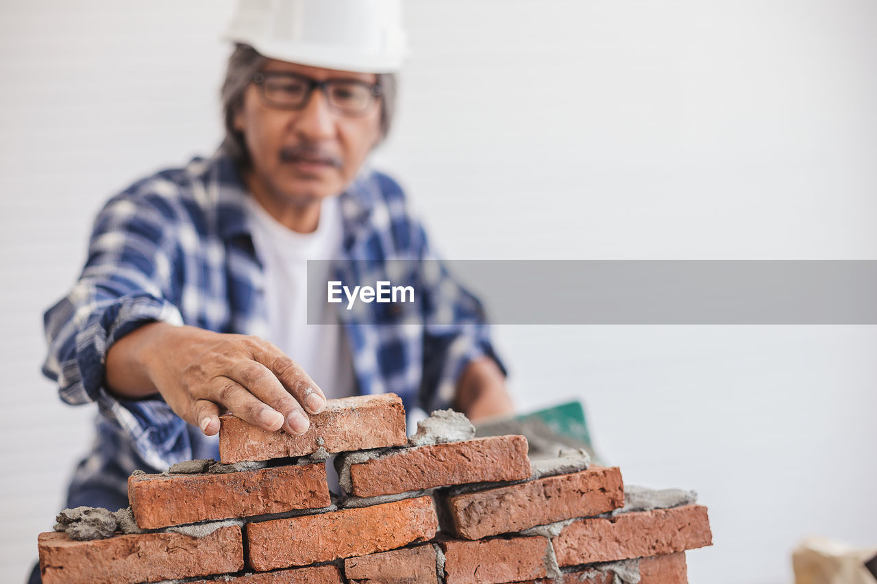 Mature man wearing hardhat making brick wall in workshop