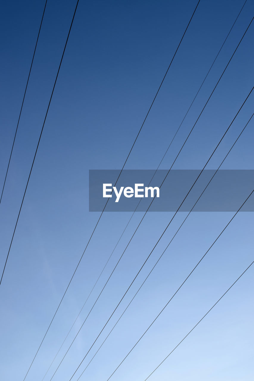 Low angle view of power cables against clear blue sky